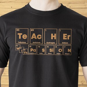 Könnte beinhalten: Schwarzes T-Shirt mit einer Grafik des Wortes "TEACHER", das mit den chemischen Symbolen für die Elemente Tellur, Actinium, Wasserstoff, Erbium, Protactinium, Schwefel, Silizium, Sauerstoff und Stickstoff ausgeschrieben ist.