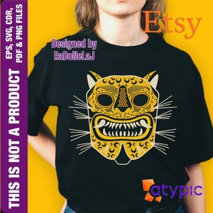 Puede incluir: Una camiseta negra con un diseño de máscara de jaguar amarilla y blanca. La máscara tiene un diseño detallado con una expresión feroz. El texto "Designed by RaDoNeLaJ" está impreso en la camiseta.