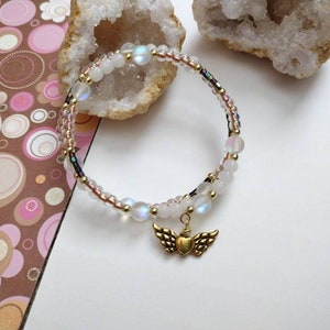 May include: A white iridescent beaded bracelet with a gold heart and wings charm.