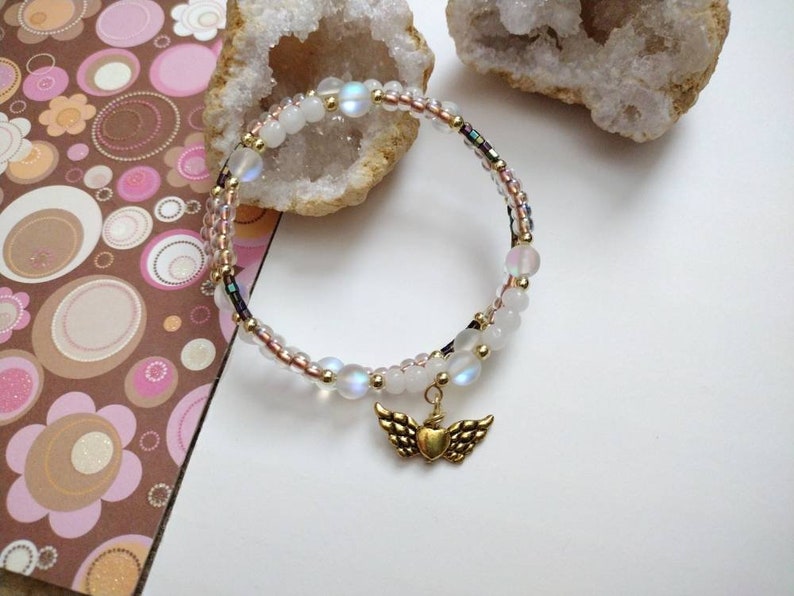 May include: A white iridescent beaded bracelet with a gold heart and wings charm.