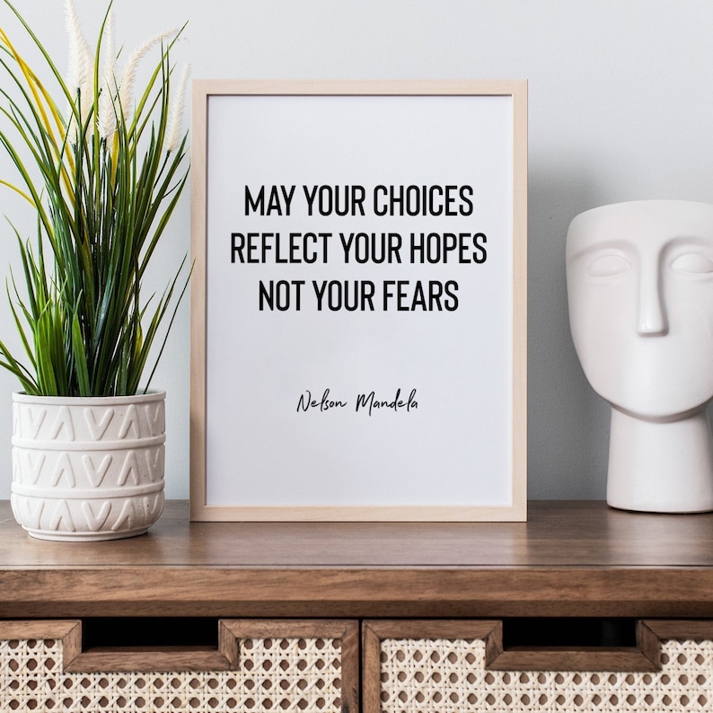 Peut inclure: Une impression encadr&eacute;e avec un fond blanc et du texte noir qui dit "May your choices reflect your hopes not your fears" avec l'auteur "Nelson Mandela" &eacute;crit en dessous. L'impression est pos&eacute;e sur une surface en bois avec une plante verte dans un pot blanc et une sculpture en c&eacute;ramique blanche &agrave; droite.