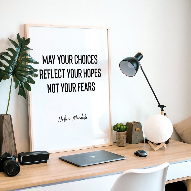 Peut inclure: Une citation inspirante encadr&eacute;e de Nelson Mandela : "Que vos choix refl&egrave;tent vos espoirs, et non vos peurs." La citation est affich&eacute;e sur un fond blanc avec du texte noir. Le cadre est en bois et a une finition brun clair. La citation est affich&eacute;e sur un bureau avec un ordinateur portable, une lampe et une plante.