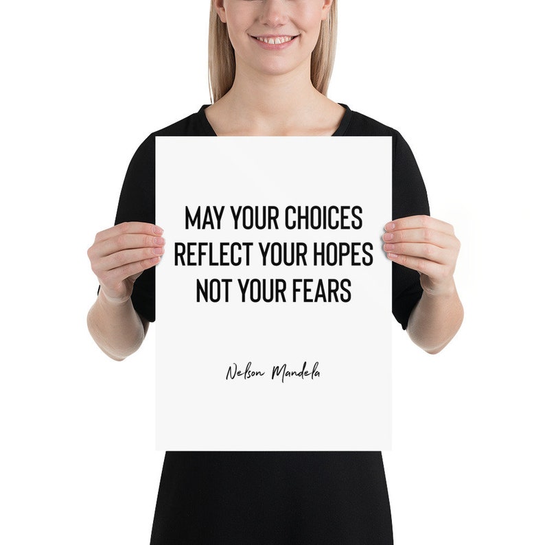 Peut inclure: Une affiche blanche avec du texte noir qui dit "May your choices reflect your hopes not your fears" et "Nelson Mandela" en cursive. L'affiche est tenue par une personne.