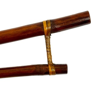 May include: A pair of brown wooden chopsticks with a yellow and brown woven band connecting them.