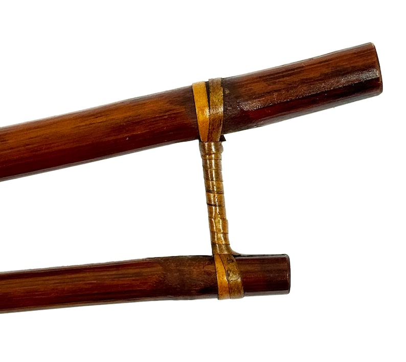 May include: A pair of brown wooden chopsticks with a yellow and brown woven band connecting them.