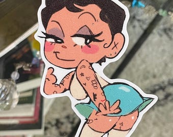 Pode incluir: Um adesivo recortado apresentando um personagem de desenho animado com cabelo curto escuro, sombra roxa e bochechas rosadas. O personagem tem tatuagens visíveis nos braços, veste um top branco e uma saia azul clara, e faz um gesto.