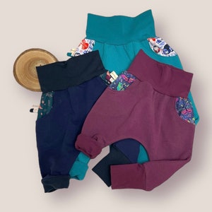 May include: Three pairs of colorful, patterned,  toddler-sized pants with a wide waistband and cuffed legs. The pants are made of a soft, stretchy fabric and have a unique design with a contrasting fabric panel on the back.
