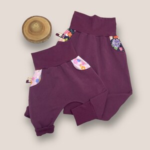 May include: Two pairs of purple  jogger pants with floral print pockets.