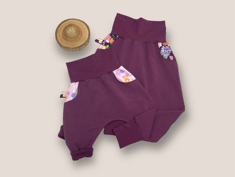 May include: Two pairs of purple  jogger pants with floral print pockets.