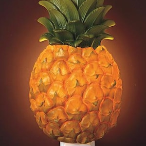 May include: A decorative night light shaped like a pineapple. The pineapple has a textured, yellow-orange body and green leafy top. The night light plugs into a standard wall outlet and emits a warm glow.