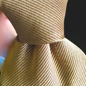 Puede incluir: Primer plano de una corbata de color dorado con un patrón tejido texturizado.
