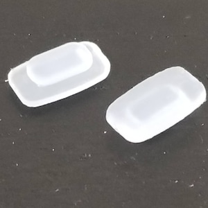 May include: Two small, white, plastic rectangular objects. One has a raised rectangular section on top. The objects are on a dark surface. The objects appear to be new.