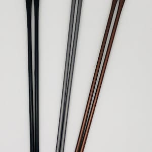 May include: Three pairs of metal chopsticks in black, gray, and bronze. Each pair has a rounded tip and a slender, straight body. The chopsticks are arranged vertically against a white background.