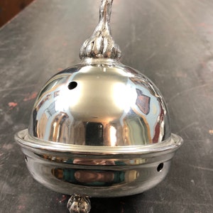 May include: A silver metal incense burner with a decorative finial on top. The burner has a round base and a domed top with a small hole in the center.