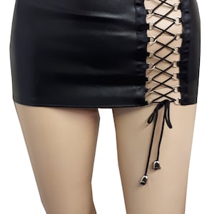 Könnte beinhalten: Ein schwarzer Kunstleder-Minirock mit seitlichem Schnürdetail und silbernen Ösen. Der Rock hat eine figurbetonte Silhouette und eine kurze Länge.