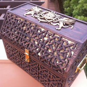 May include: A dark wood treasure chest with intricate carvings and gold accents. The chest features a skull and crossbones design with two winged creatures on either side.