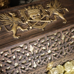 May include: A wooden treasure chest with a gold-colored skull and crossbones design on the lid. The chest is decorated with intricate carvings and has a gold-colored latch.