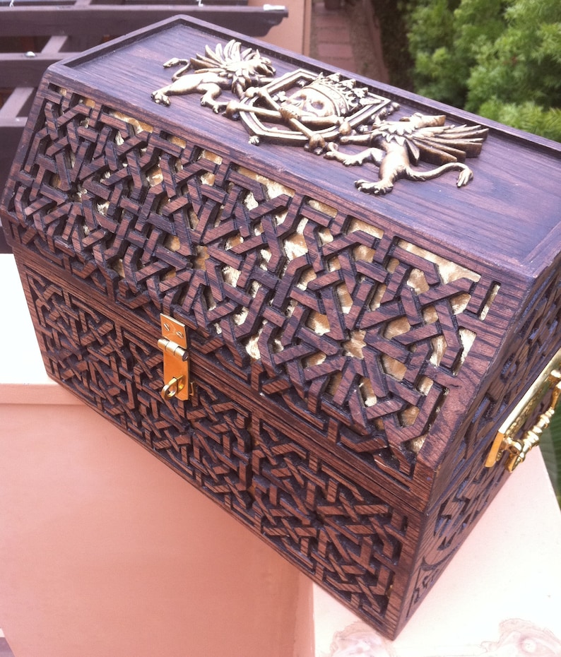 May include: A dark wood treasure chest with intricate carvings and gold accents. The chest features a skull and crossbones design with two winged creatures on either side.