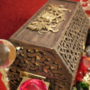 May include: A wooden treasure chest with intricate carvings and a gold-colored design on the lid. The chest is open and filled with colorful gems and jewels.