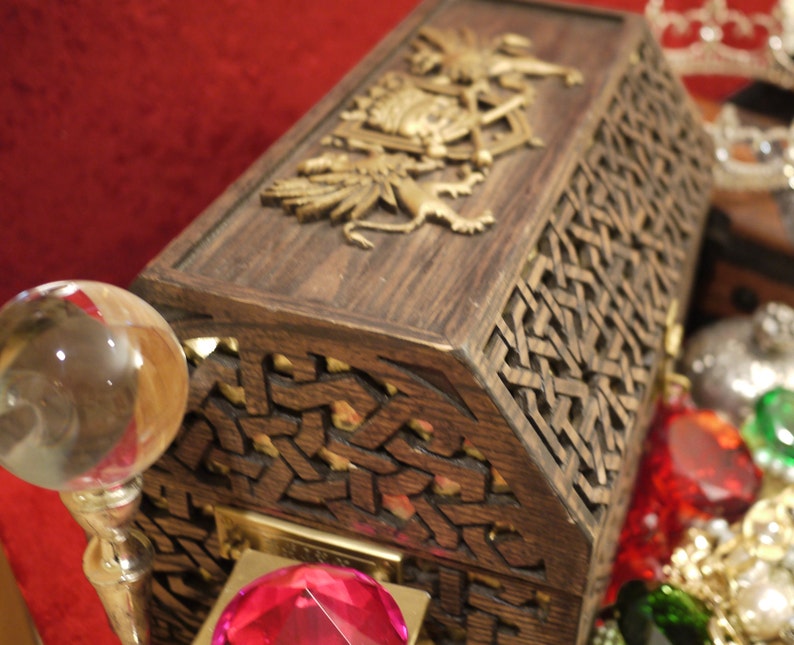 May include: A wooden treasure chest with intricate carvings and a gold-colored design on the lid. The chest is open and filled with colorful gems and jewels.