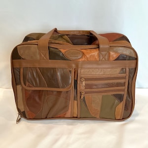 Puede incluir: Bolso de viaje vintage de cuero patchwork en tonos marrón, beige y naranja. El bolso tiene dos asas superiores, múltiples compartimentos con cremallera y un bolsillo frontal. La marca "Traders" es visible.
