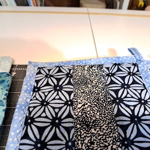 May include: Close-up of a handmade quilt with various blue and white patterned fabrics. The quilt features a light blue polka dot border with a scalloped edge. The central panels display floral and abstract designs.