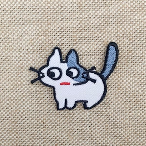 May include: White and grey embroidered iron-on patch of a cartoon cat with big eyes and a surprised expression.