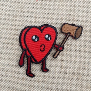Pode incluir: Um personagem vermelho em forma de coração com um rosto bonito e olhos grandes segura um pequeno martelo marrom. O personagem tem pernas e braços pequenos.