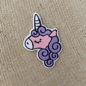 May include: A purple and pink embroidered unicorn patch with a white horn. The unicorn has closed eyes and a curled mane.