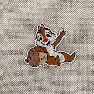 May include: An embroidered patch featuring Chip from Disney's Chip 'n Dale Rescue Rangers. Chip is sitting on an acorn and waving with his right paw.