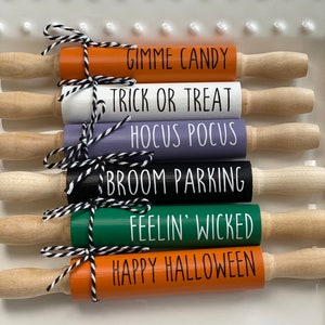 May include: Six wooden rolling pins with Halloween themed sayings. The sayings are "Gimme Candy", "Trick or Treat", "Hocus Pocus", "Broom Parking", "Feelin' Wicked", and "Happy Halloween".