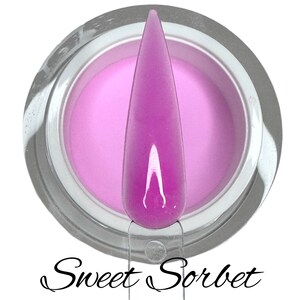 Puede incluir: Un pequeño frasco de polvo para uñas de color morado claro con una uña sumergida en el polvo. El frasco tiene una tapa plateada y el texto "Sweet Sorbet" está escrito debajo del frasco.