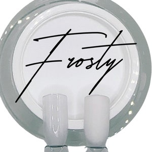 Puede incluir: Dos botellas de esmalte de u&ntilde;as de vidrio transparente con un esmalte blanco opaco en su interior. Las botellas est&aacute;n sobre una superficie blanca con la palabra "Frosty" escrita en cursiva negra.