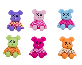 Könnte beinhalten: Sechs kleine Plüschbären in einem Farbschema aus Rosa, Blau, Lila, Grün, Orange und Magenta. Jeder Bär trägt ein rosa-weiß gemustertes Hemd mit den Buchstaben "XX" auf der Brust.