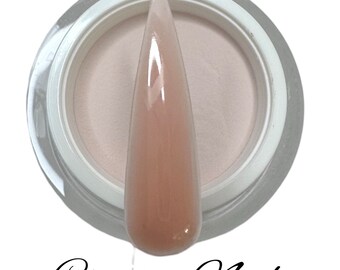 Könnte beinhalten: Ein klares Glas mit weißem Deckel, gefüllt mit hellem rosa Acrylpulver. Im Vordergrund ist ein hellrosa Nageldip zu sehen. Der Text "Creamy Nude" steht unter dem Glas.