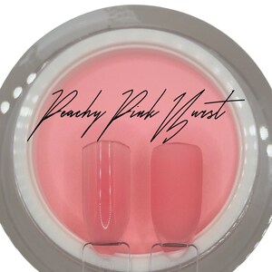 Puede incluir: Dos botellas transparentes de esmalte de u&ntilde;as de color rosa melocot&oacute;n. Las botellas est&aacute;n sobre una superficie blanca con un fondo rosa. El texto "Peachy Pink Burst" est&aacute; escrito en negro sobre el fondo.
