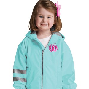 May include: A light blue hooded jacket with reflective strips on the sleeves and a pink monogram on the front. The jacket has a zipper closure and a hood.
