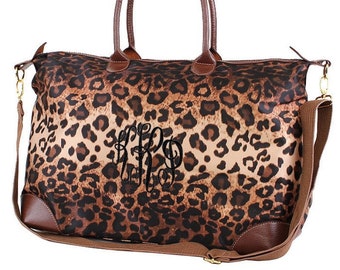 Può includere: Una borsa da viaggio marrone e beige con stampa leopardata, con manico e tracolla in pelle marrone. La borsa è monogrammata "LRB" con ricamo nero.