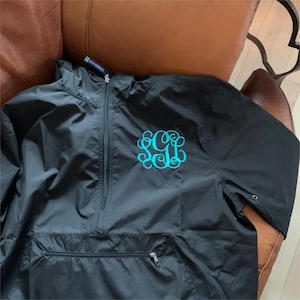 May include: Black hooded jacket with a teal monogram on the front. The jacket has a zipper closure and a kangaroo pocket.