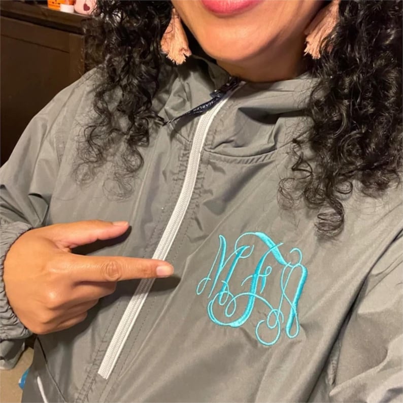 May include: A gray hooded jacket with a white zipper and a teal blue monogram on the front. The monogram is the letters "MFA" in a cursive font.