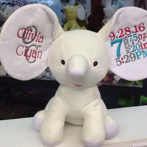Op de afbeelding: Witte pluche olifant knuffel met geborduurde oren. Het ene oor zegt "Olivia Cyan" en het andere oor zegt "9.28.16 7 pond 7,5 oz 20 inch 5:29 PM".