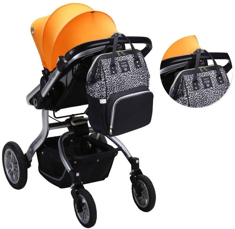 May include: A black and white leopard print diaper bag with gold accents is attached to a silver stroller with an orange canopy. The stroller has a black basket underneath.