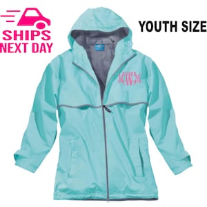 May include: A light blue youth-sized rain jacket with a gray zipper and a gray hood. The jacket has a pink monogram on the front.  YOUTH SIZE is written in black text at the top of the image.