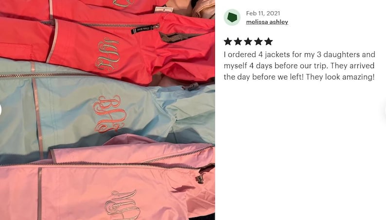 May include: Three rain jackets in bright coral, light blue, and soft pink, each featuring a silver-toned zipper and a decorative embroidered monogram on the chest. The jackets are layered vertically, showcasing the smooth fabric and stitching.