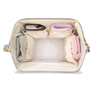 K&ouml;nnte beinhalten: Eine graue Wickeltasche mit mehreren F&auml;chern und Taschen. Die Tasche ist offen und mit verschiedenen Babyartikeln gef&uuml;llt, darunter Windeln, Feuchtt&uuml;cher und eine Wickelunterlage.
