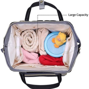 May include: A gray and black diaper bag with a large capacity. The bag is open and filled with various baby items, including a rolled up blanket, a baby toy, and a container of baby formula.