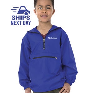 May include: A royal blue hooded jacket with a zipper closure and a small pocket on the front. The jacket has a name embroidered on the front: "Nicholas".