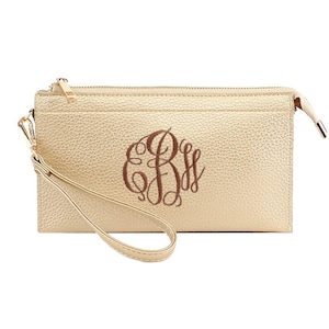 Op de afbeelding: Een gouden clutch met een ritssluiting en een polsbandje. De clutch heeft een monogram met de initialen "E.B.S." in bruin garen.