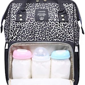 May include: A black and white leopard print diaper bag with a zippered top and multiple pockets. The bag has three insulated bottle holders and a mesh pocket inside. The bag has a black handle and a black adjustable shoulder strap. The bag has a label that says "LEQUEEN COMPO EVINHO, AMADA-SE CAMINHO, SINCE 1989".