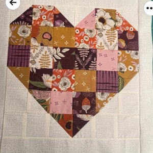 May include: A patchwork heart quilt with a variety of floral and geometric patterns in shades of brown, pink, orange, and white. The quilt is made of squares and triangles, and the heart shape is outlined in a darker brown fabric.